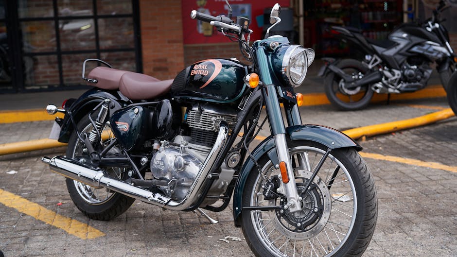 A person wearing a black helmet, black face mask, and dark clothing is sitting on a black motorcycle on a paved road with a grassy verge and a sidewalk on the right side. The motorcycle is positioned centrally in the image, with the rider holding the handlebars. In the background, there are trees, utility poles with power lines, and a slightly foggy or hazy sky, suggesting early morning or late afternoon lighting. The scene appears to be in a suburban or semi-rural area. This image relates to the logistics of home relocation or moving services, such as coordinating transport or delivery of furniture and household items with companies like Enfield Man and Van, who provide removal services in Enfield.